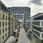 A vibrant urban street flanked by modern and historic buildings under a cloudy sky.