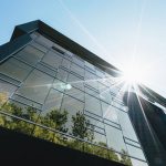 Low angle view of a modern skyscraper with reflections and sun flare, emphasizing contemporary architecture.
