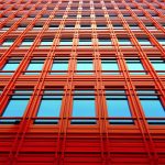 Low angle shot of a modern red building with glass windows reflecting the sky.