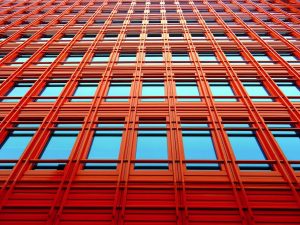 Low angle shot of a modern red building with glass windows reflecting the sky.